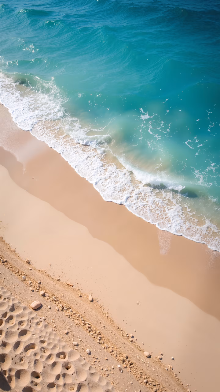 Aerial view of a sandy beach meeting turquoise ocean waters, bathed in soft sunlight.