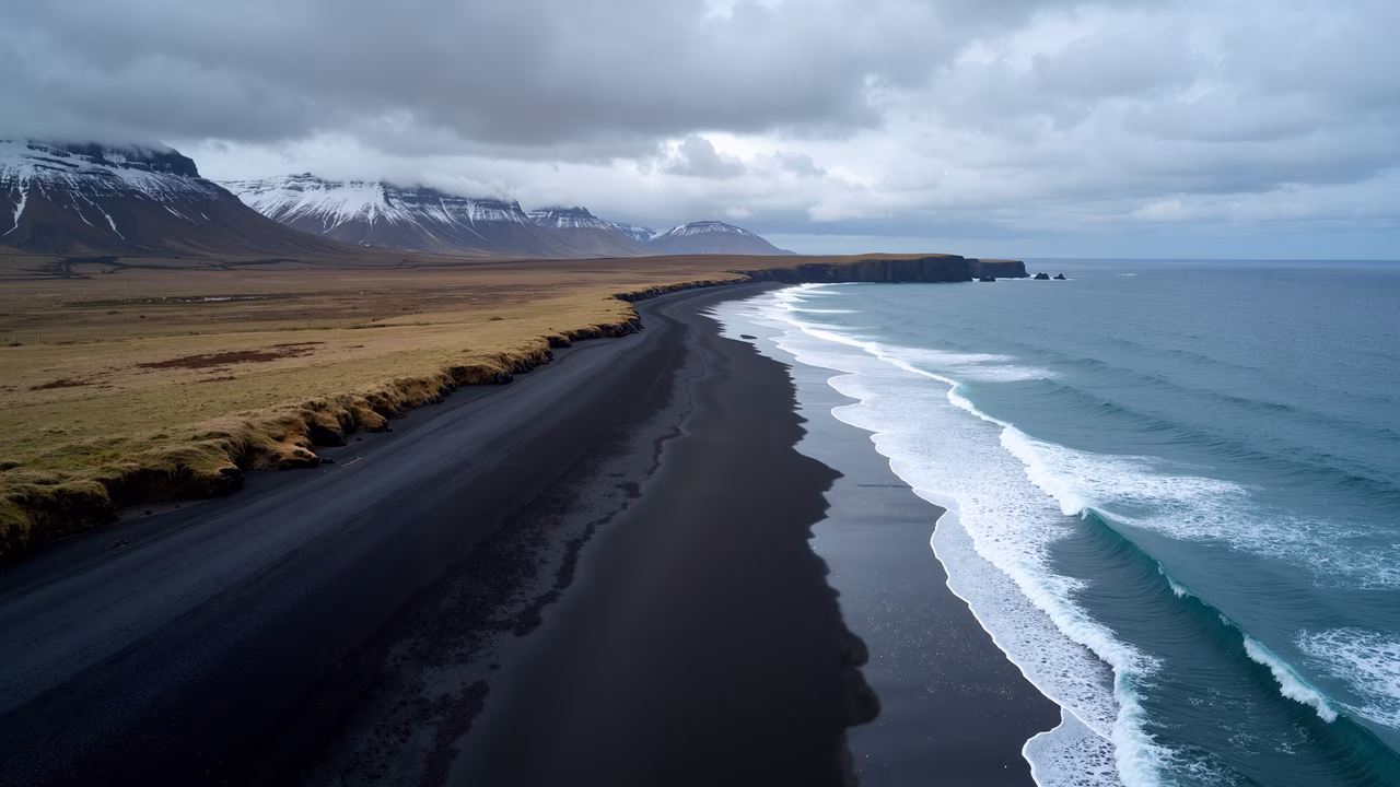 A stunning black sand beach with turquoise waves and rugged mountains under a cloudy sky.