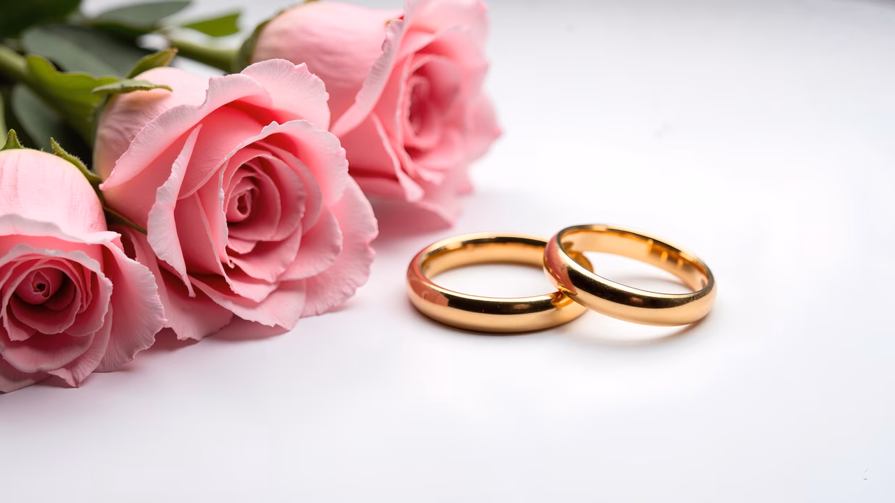 Golden wedding rings intertwined with pink roses, symbolizing love and commitment.