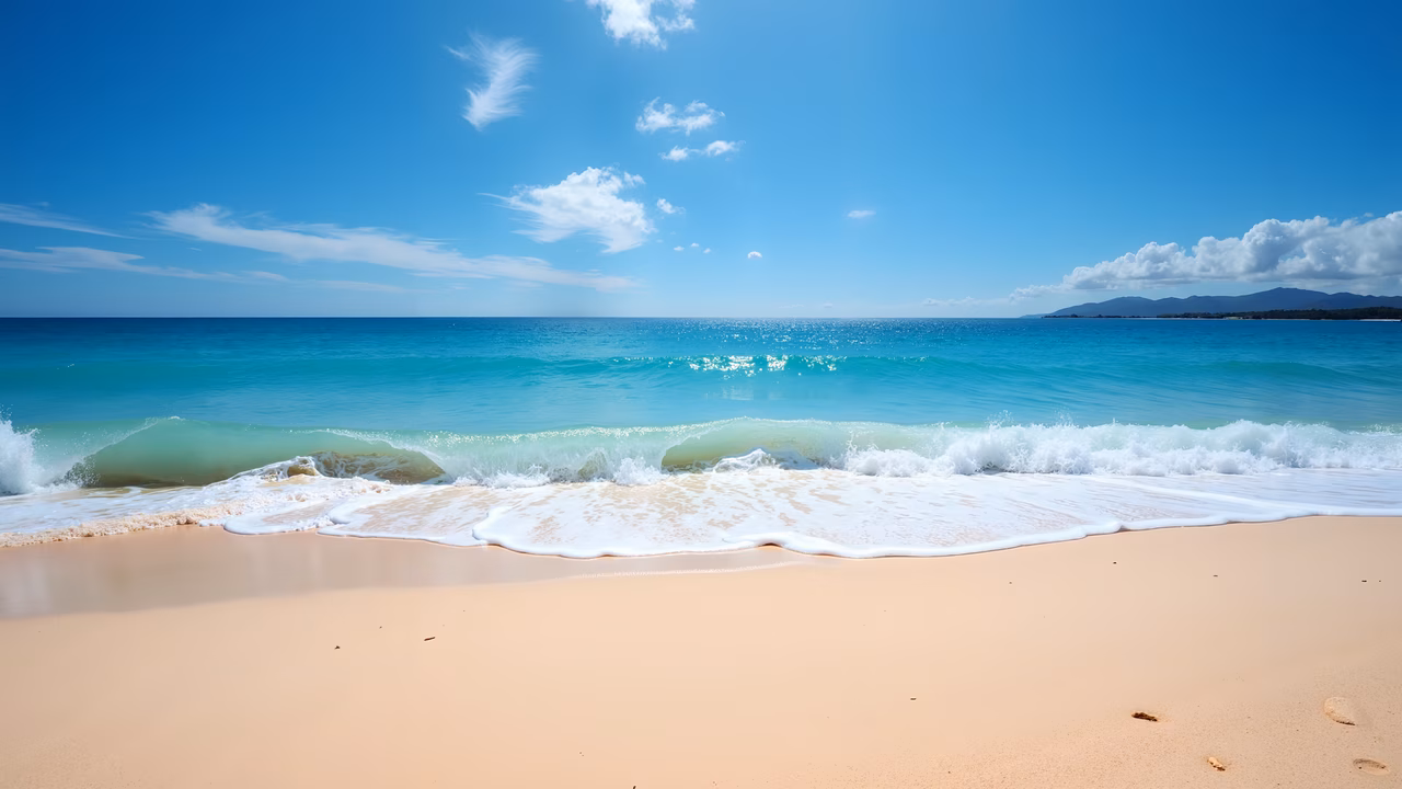 A peaceful beach with soft pink sand and turquoise ocean waves under a clear blue sky with scattered clouds.