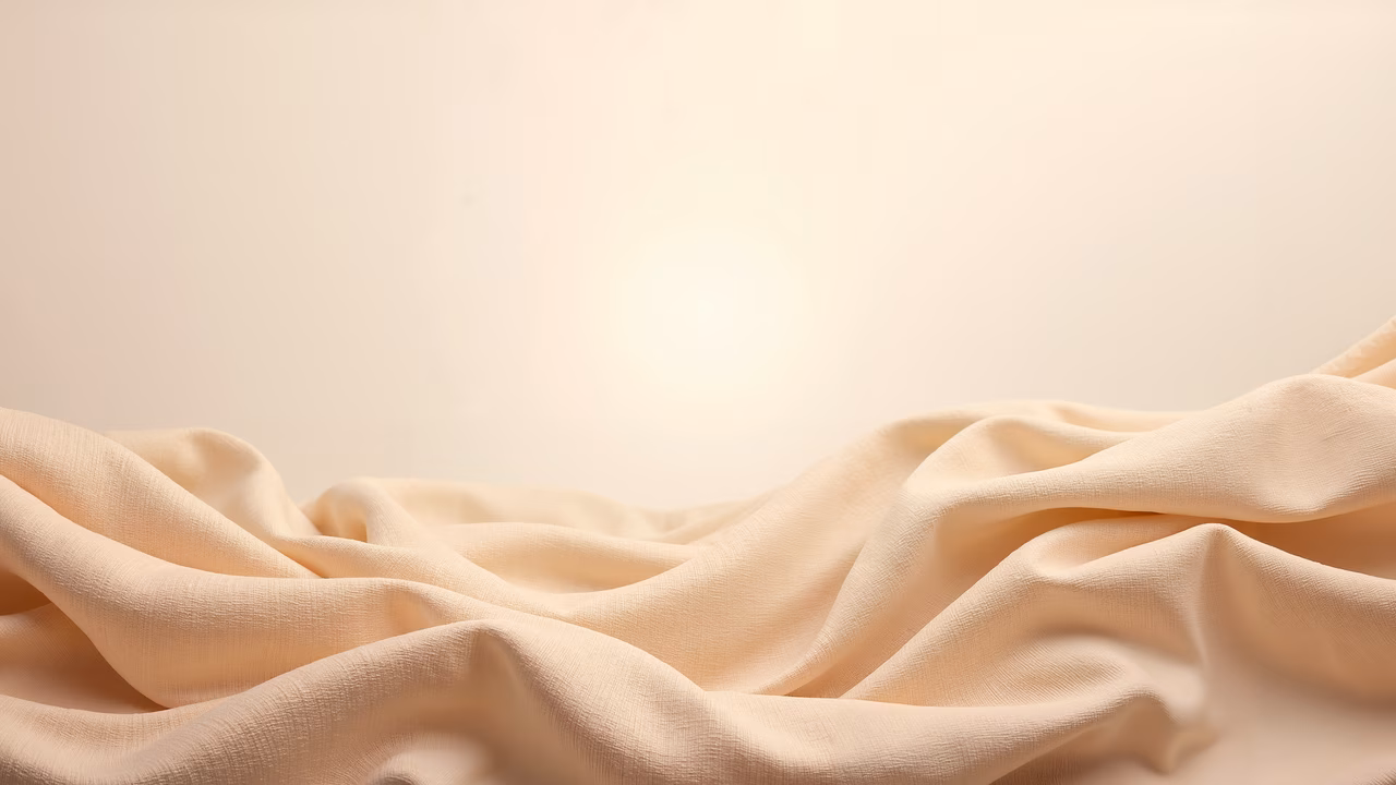 Close-up of soft, light beige fabric with intricate folds and creases, highlighting texture and depth.
