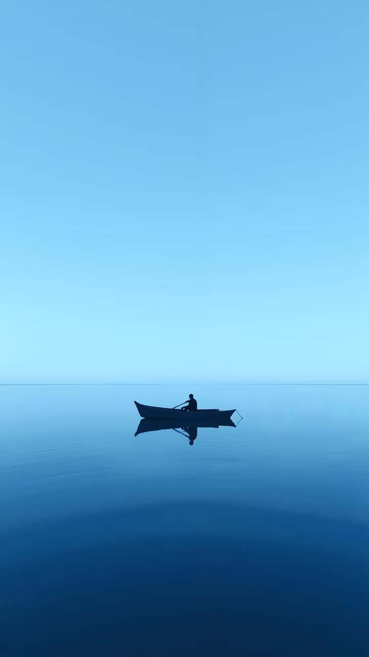 A solitary figure in a boat on a calm sea under a clear blue sky.