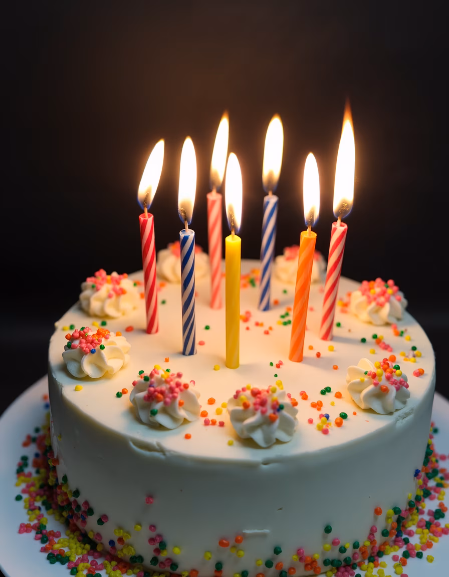 Close-up of a birthday cake with colorful sprinkles and lit candles.