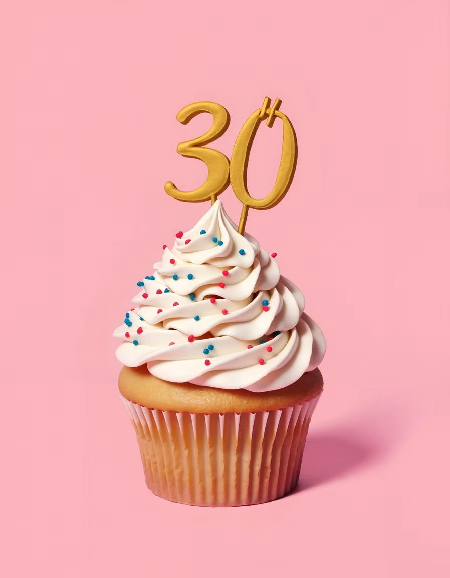 Festive cupcake with colorful sprinkles and golden '30' decoration on pink background.