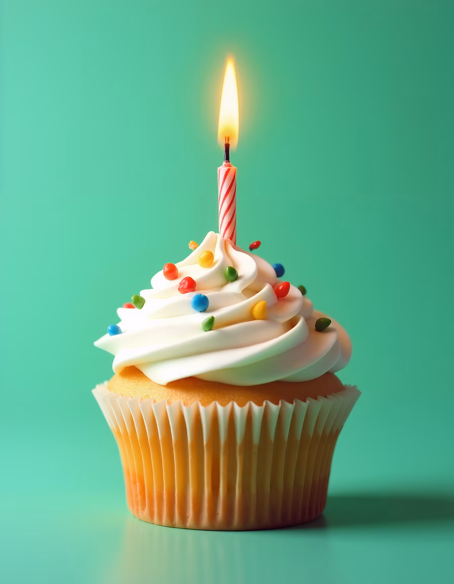 Close-up of a festive cupcake with a lit candle on a teal background.