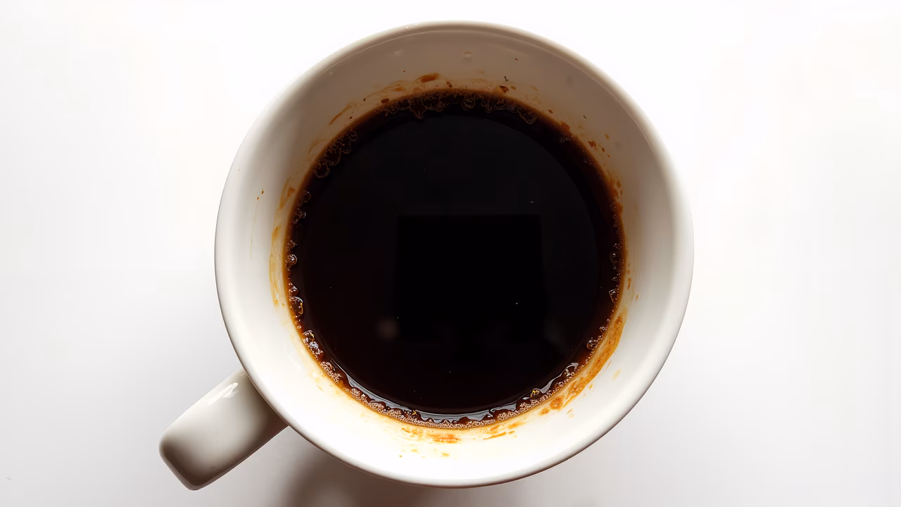 Close-up of a white ceramic cup filled with dark coffee on a bright white background.