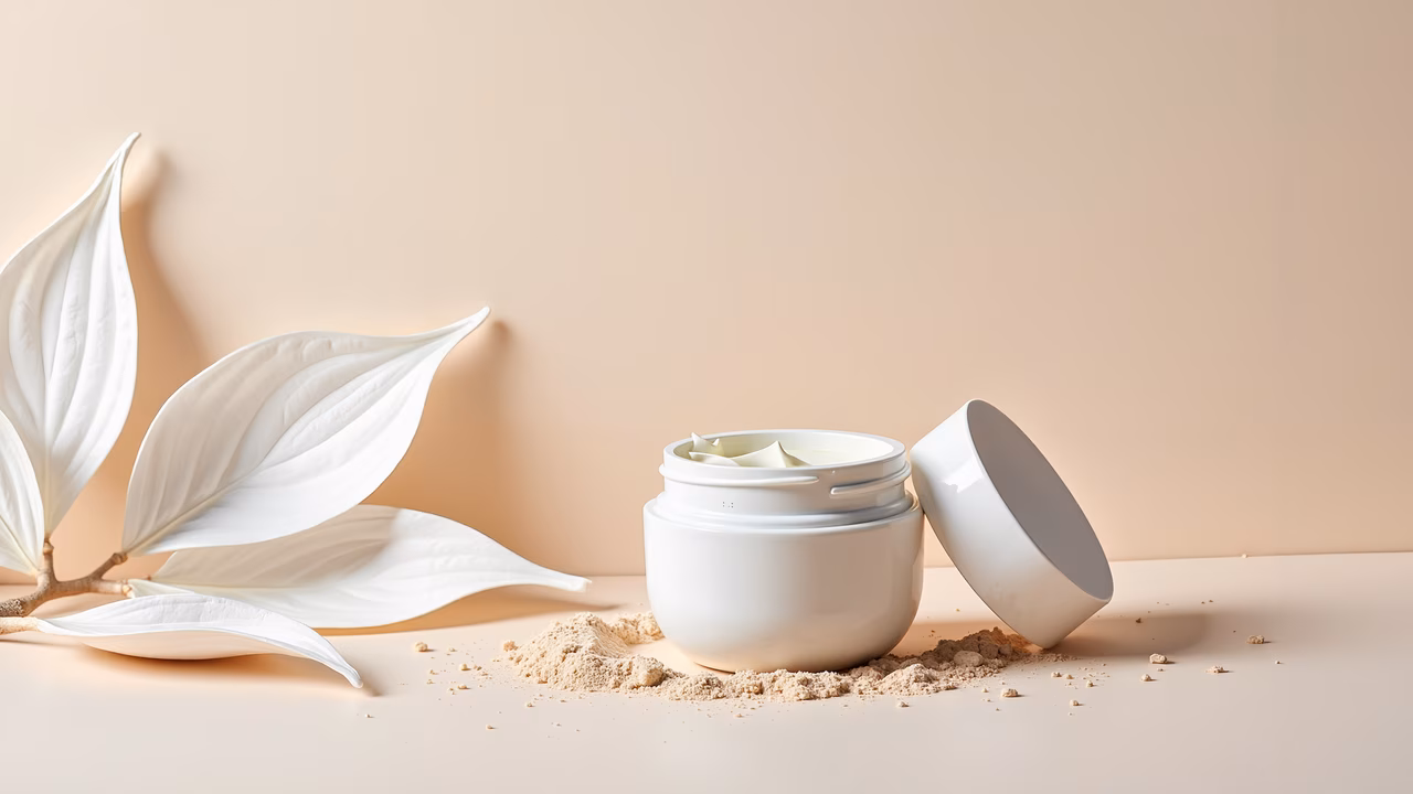 Close-up of a cream jar with powder and leaves, minimalist beauty shot.