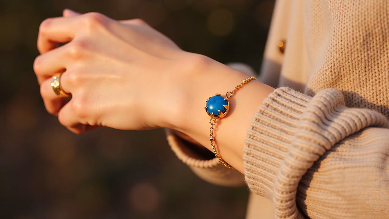 Close-up of a hand wearing a golden ring and blue stone bracelet, illuminated by warm sunlight.