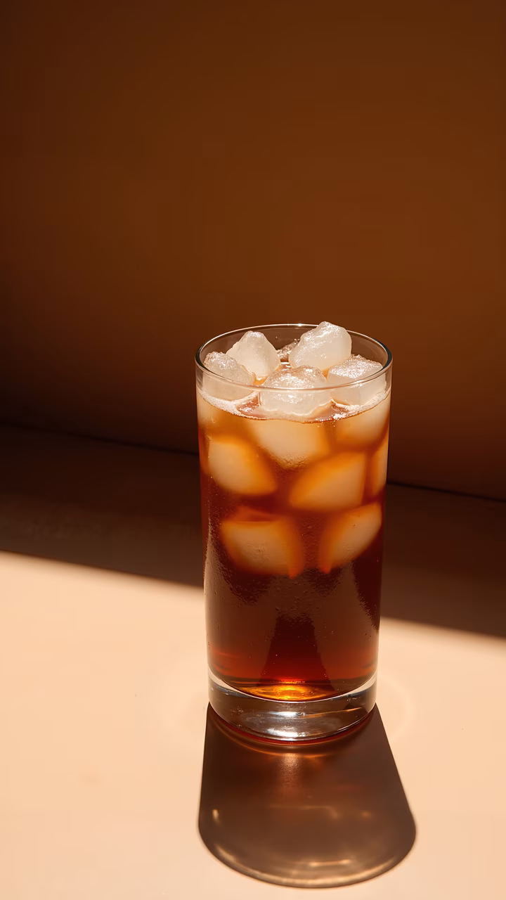 A refreshing iced coffee beverage with ice cubes, set against a warm backdrop.