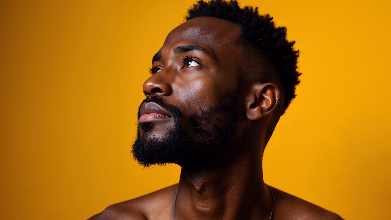 Close-up portrait of a man with a beard, looking up against a yellow background.