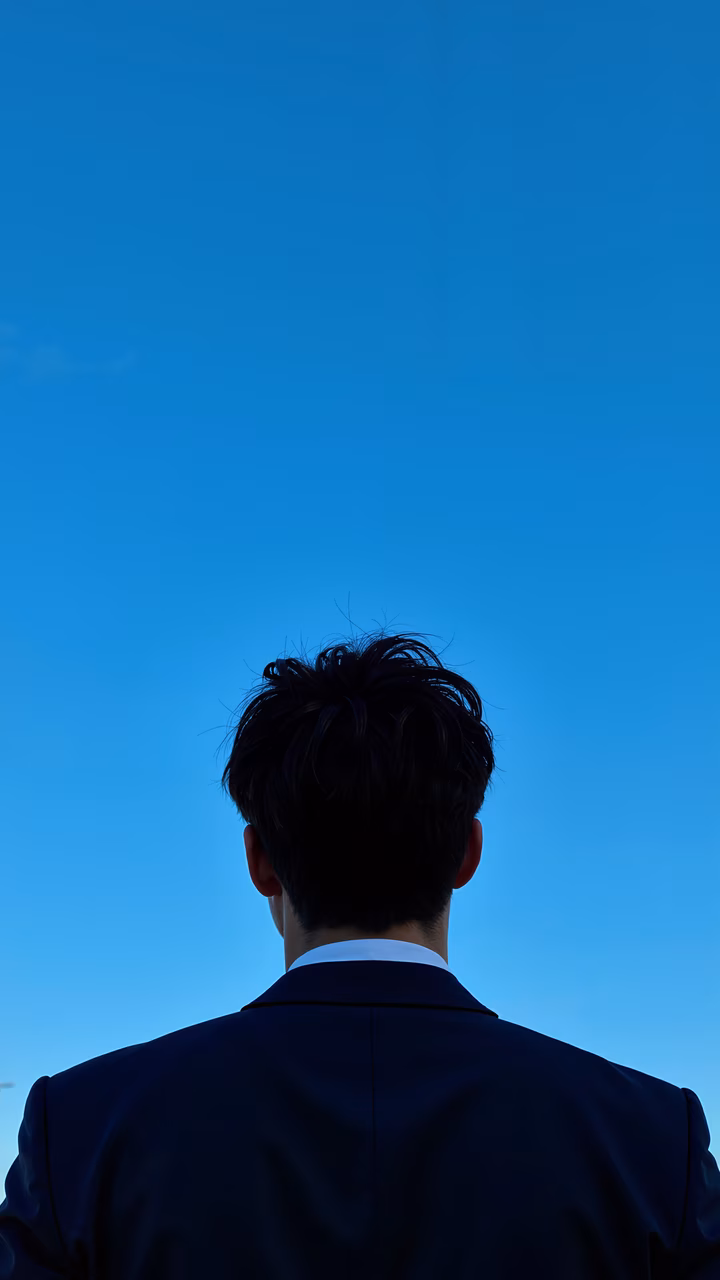 Silhouette of a man in a suit against a blue sky, evoking solitude and contemplation.