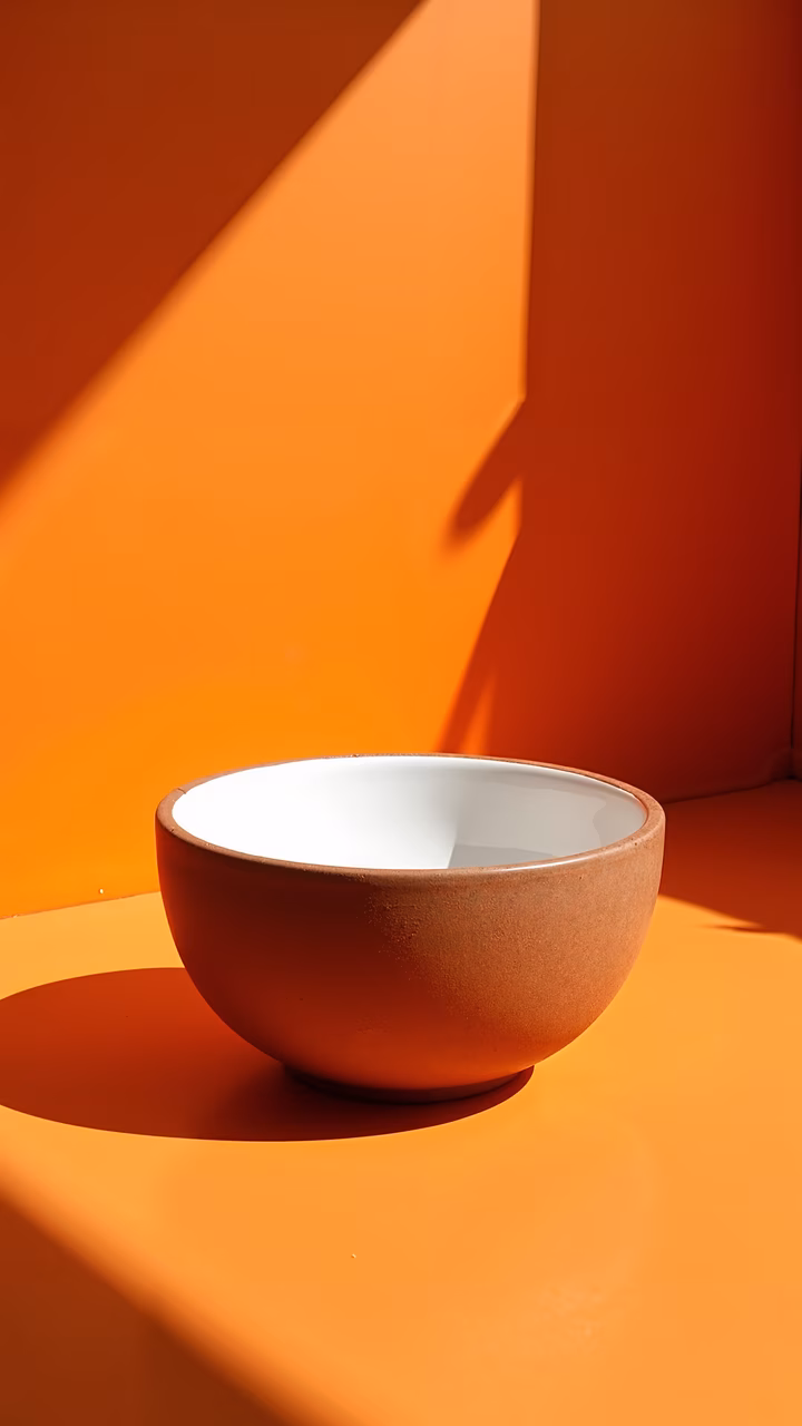 Minimalist bowl with white interior on vibrant orange background, emphasizing textures and colors.