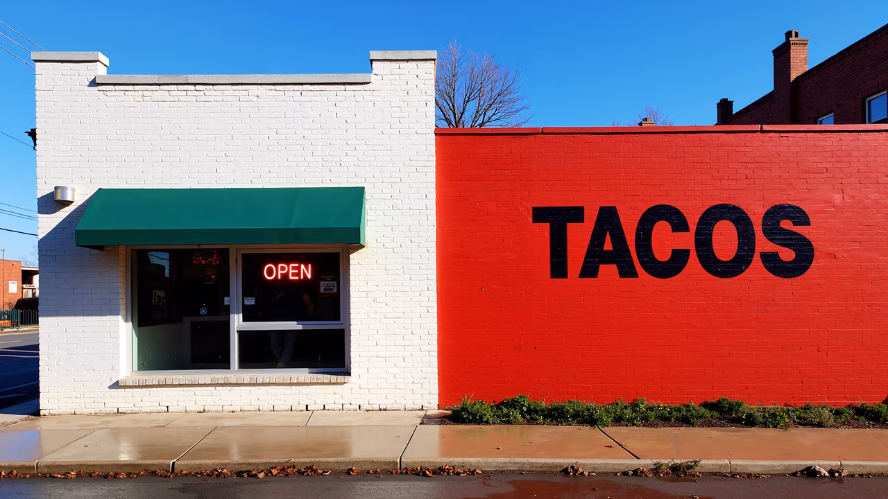 Bright red brick wall with bold 'TACOS' sign, open neon sign, clear blue sky, autumn day.