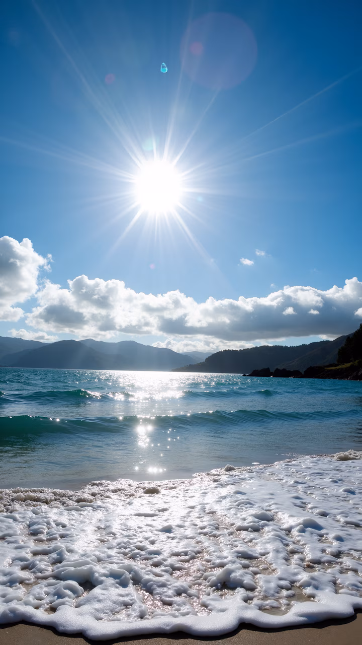 Golden sunlight illuminates a peaceful beach with frothy waves and sandy shores.