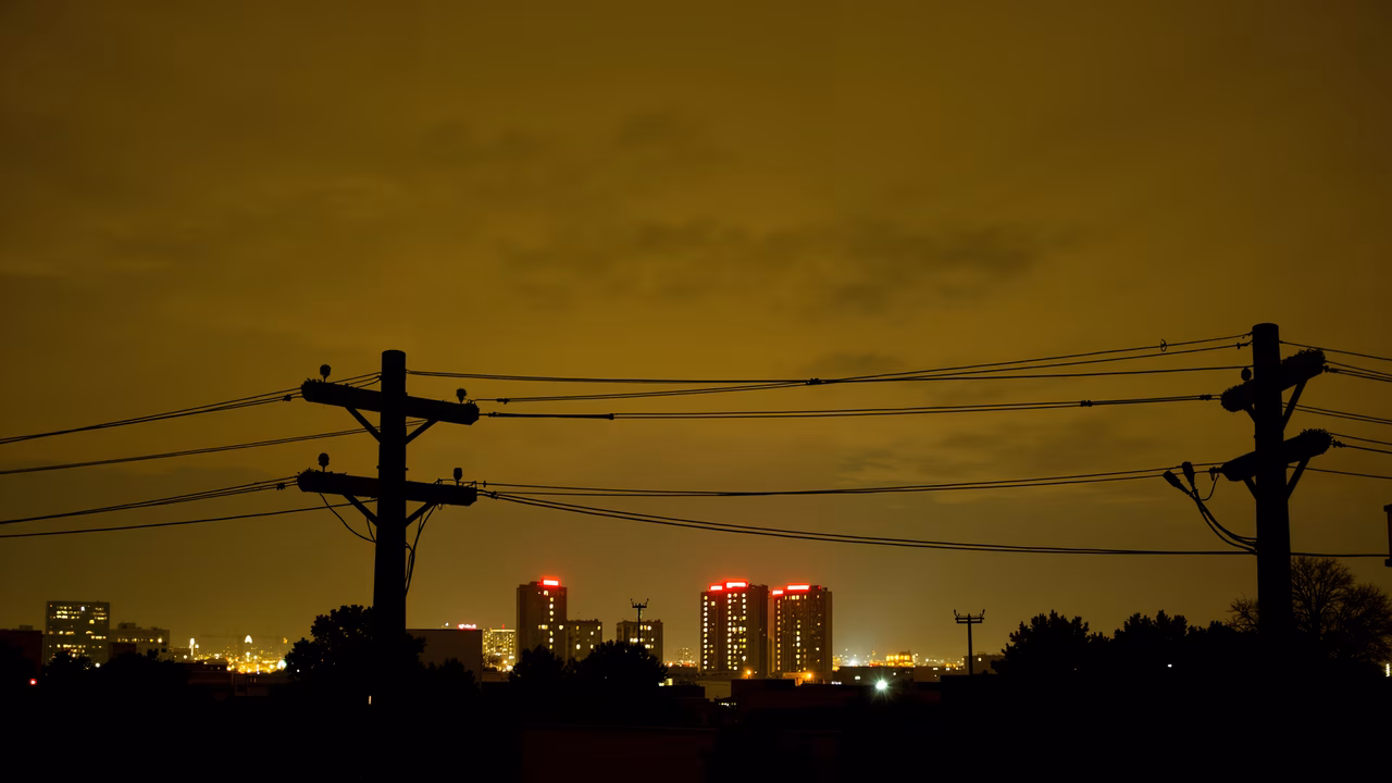 Silhouetted cityscape with glowing red lights and utility poles at night.