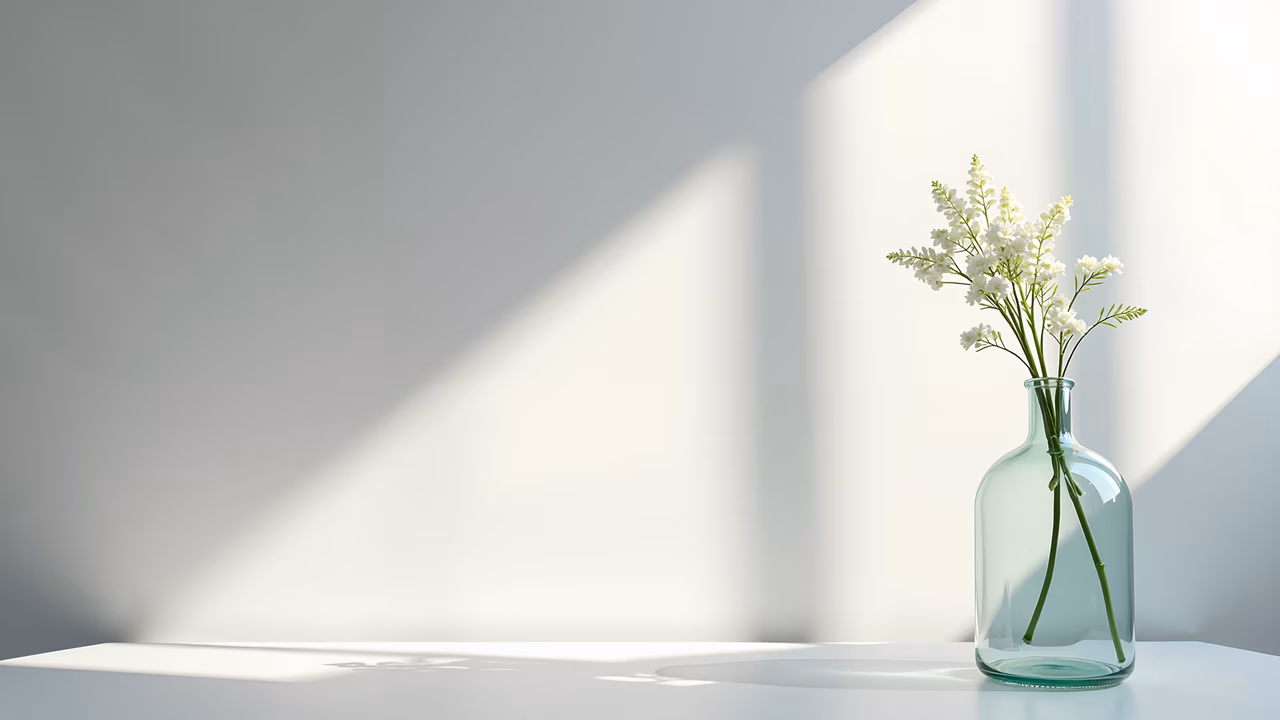 Minimalist still life with white flowers in a glass bottle, bathed in soft natural light.