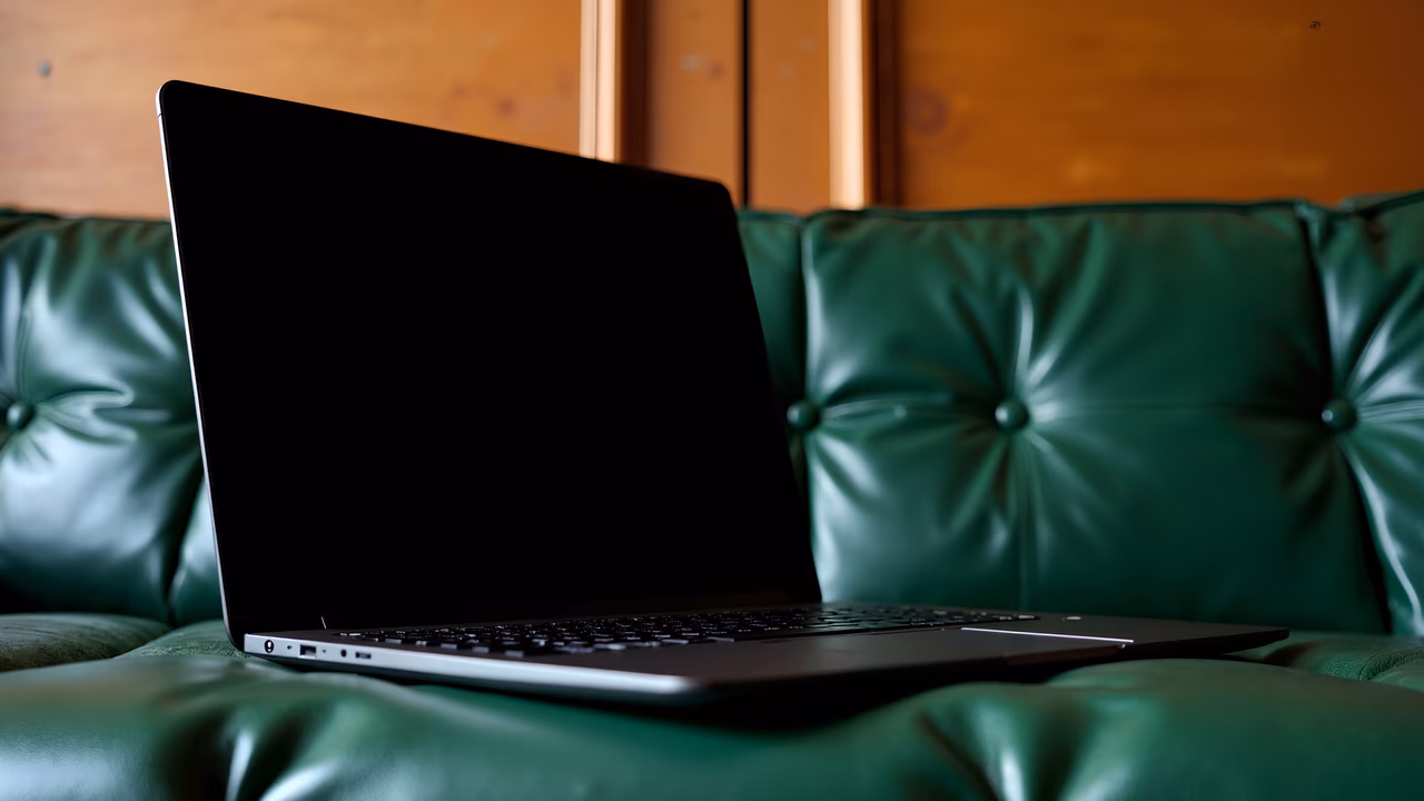 Sleek laptop on a green leather couch in a cozy interior setting.
