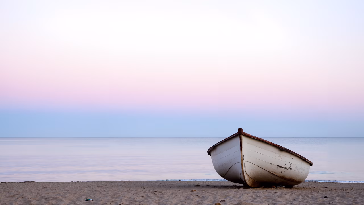 A peaceful sunset scene with a lone boat on the beach.