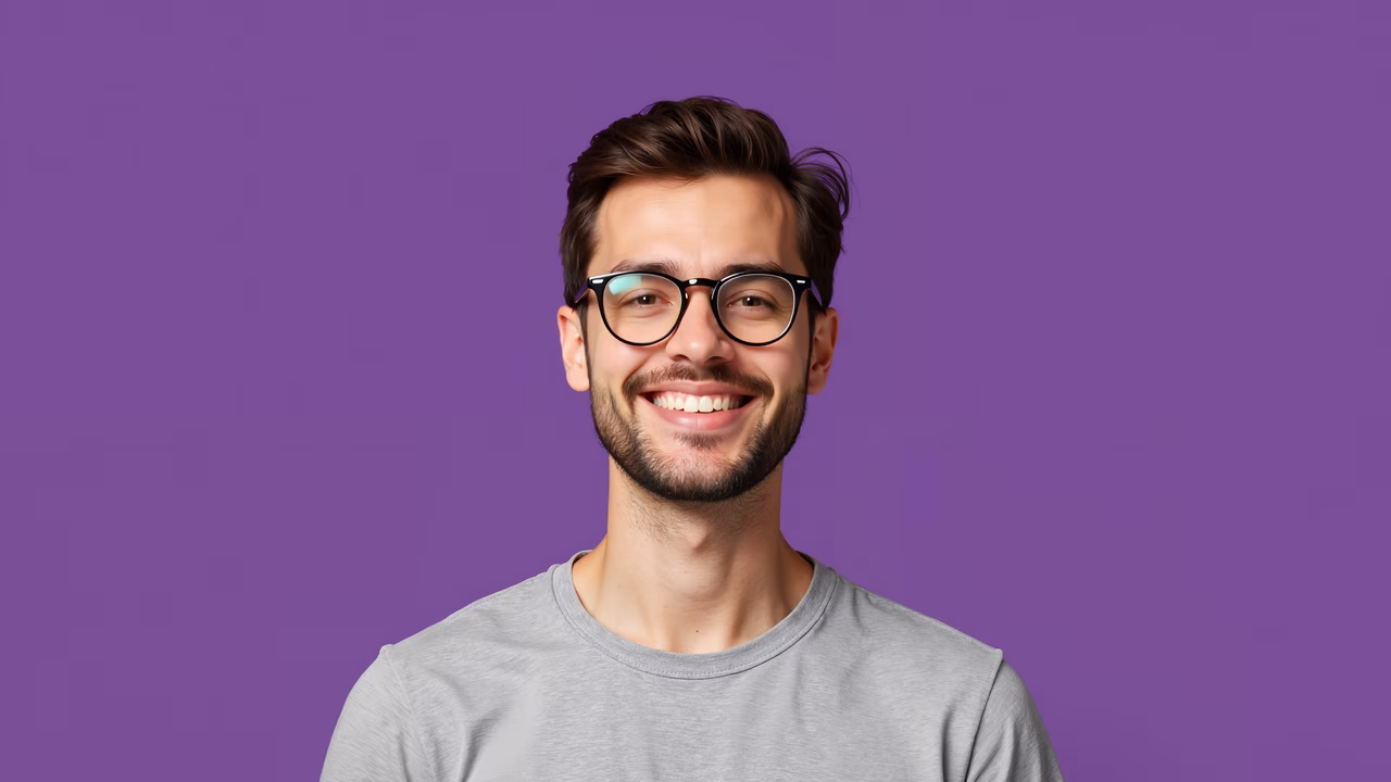 Close-up portrait of a smiling man with glasses against a purple backdrop.