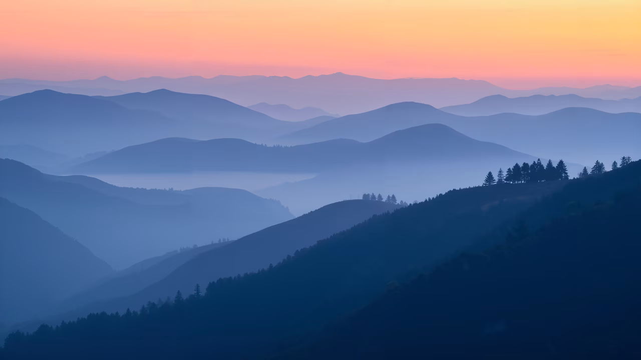 A tranquil mountain landscape at dawn, featuring misty peaks and evergreen trees.