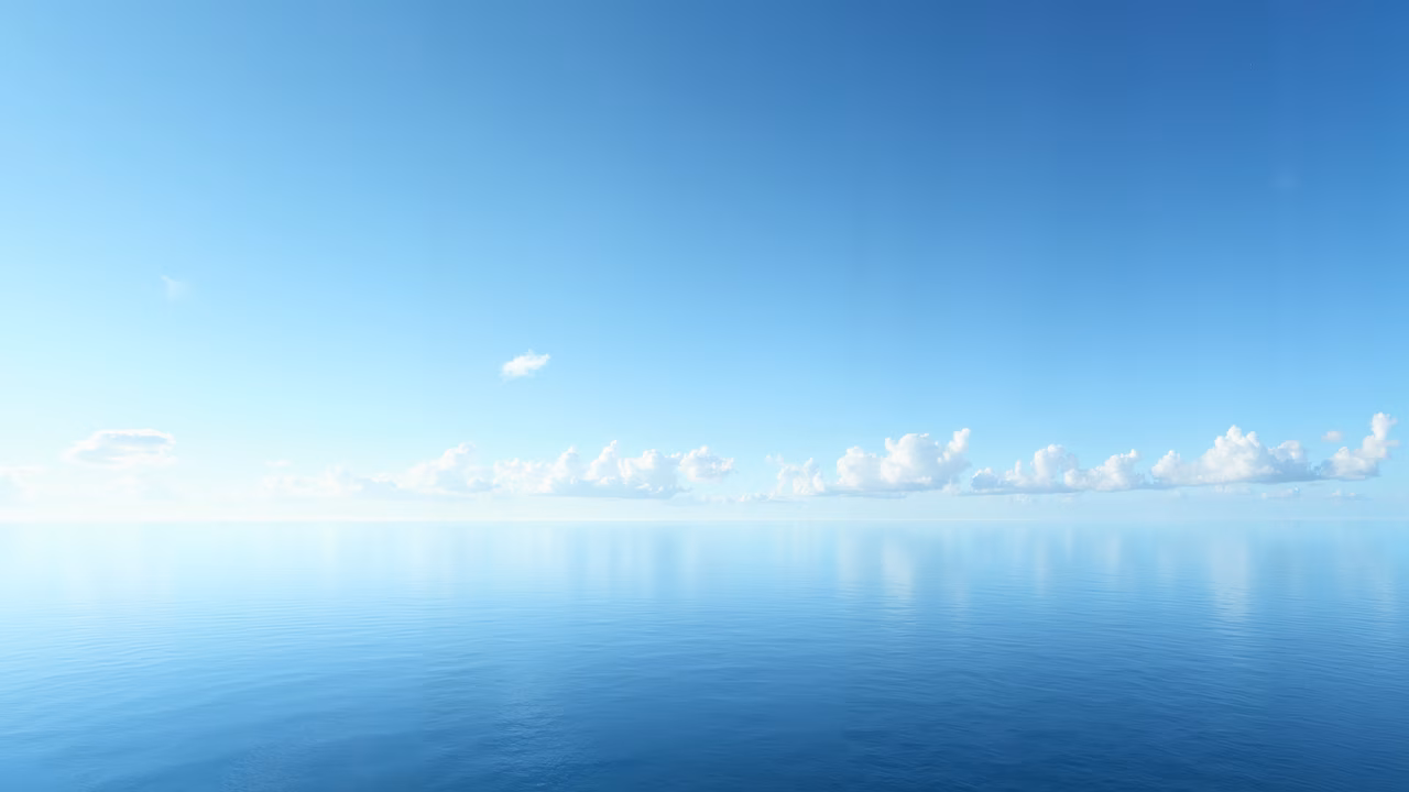 Calm ocean under a clear blue sky with scattered clouds.