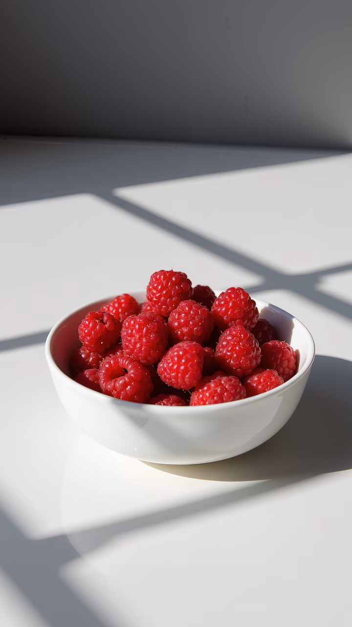 Close-up of fresh raspberries in a white bowl, illuminated by soft natural light.
