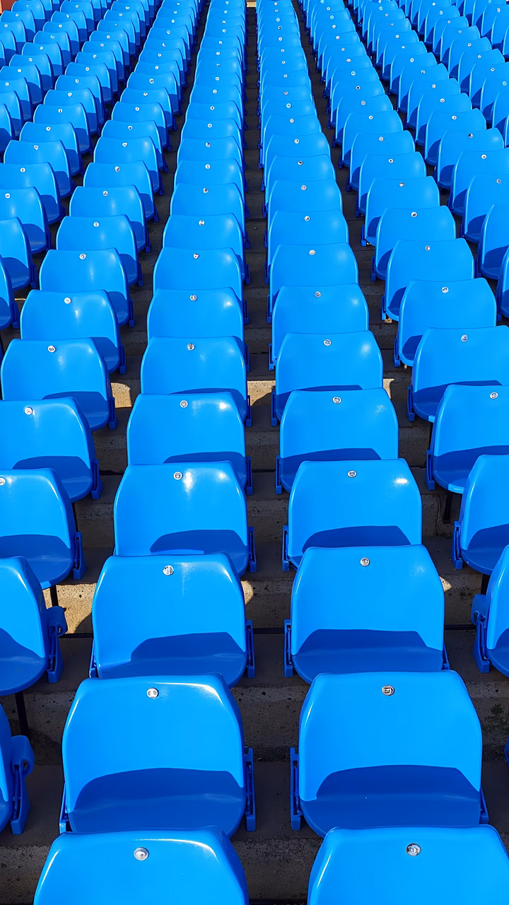 Rows of blue stadium seats under bright sunlight, creating a sense of anticipation.