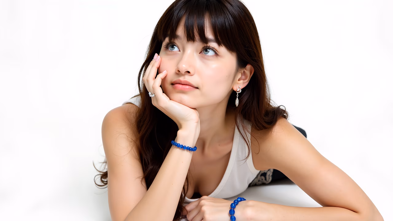 Serene portrait of a young woman in contemplation, wearing blue jewelry against a white backdrop.