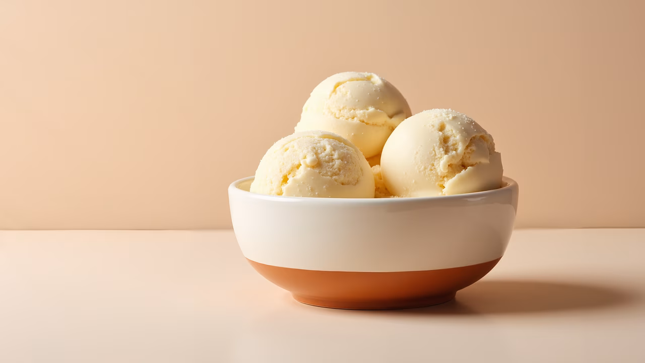 Close-up of vanilla ice cream in a white bowl with a terracotta rim, set against a neutral beige background.