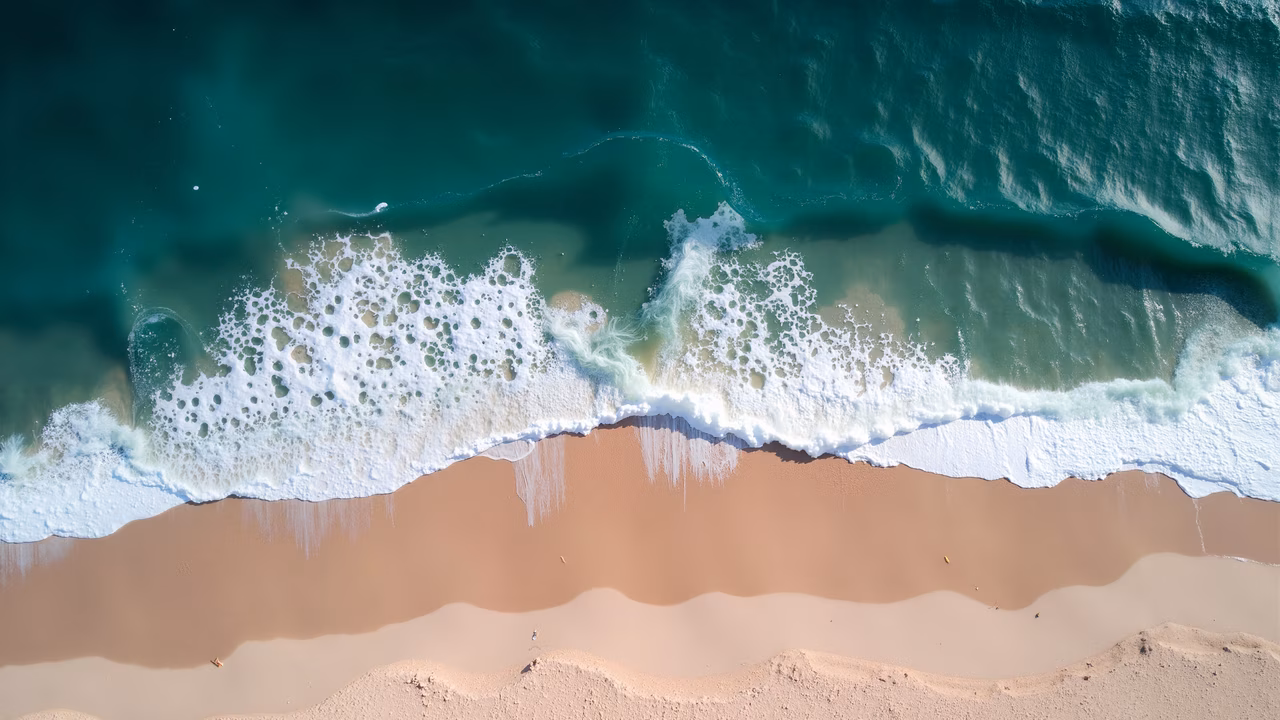 Aerial view of turquoise ocean waves meeting sandy beach