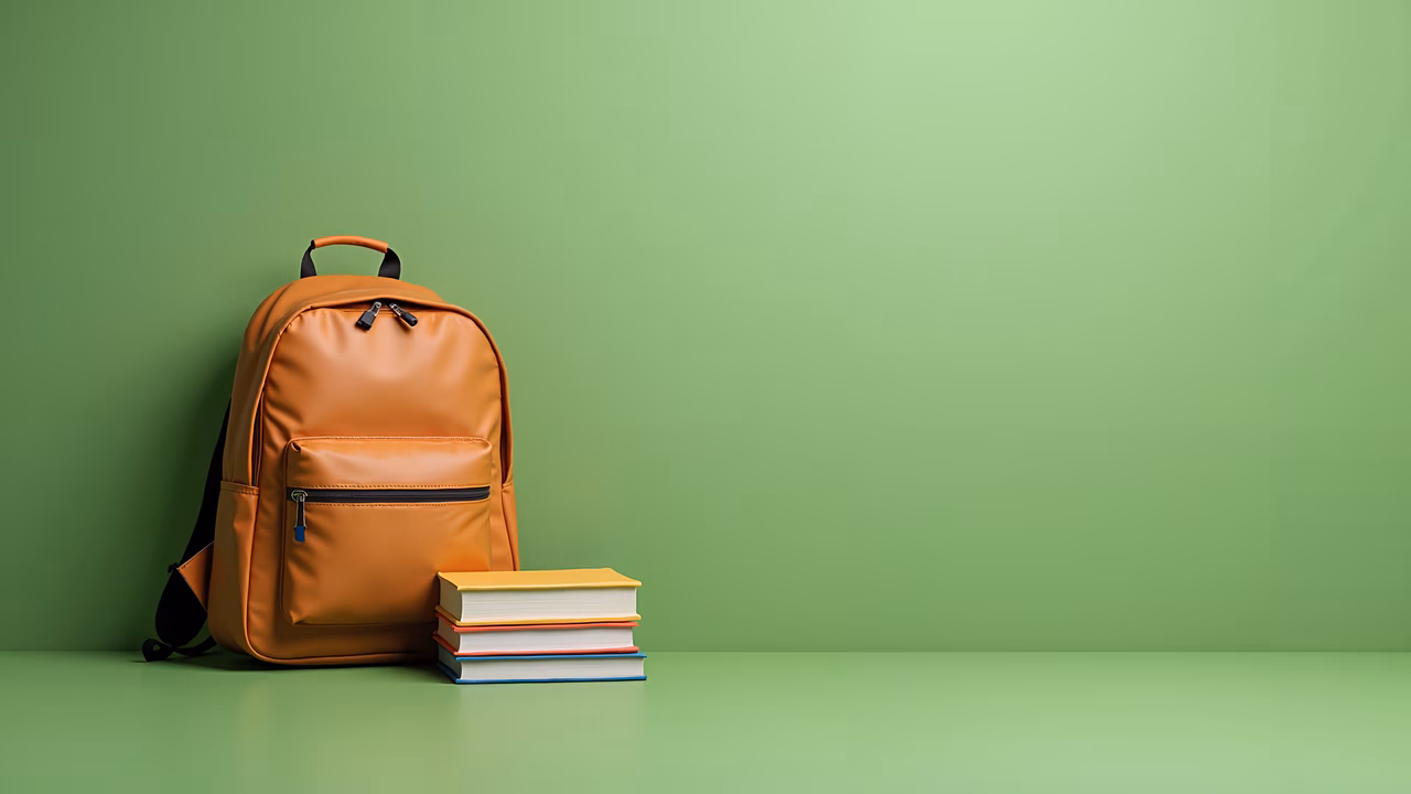 Orange backpack and books on a green background, symbolizing education and readiness.