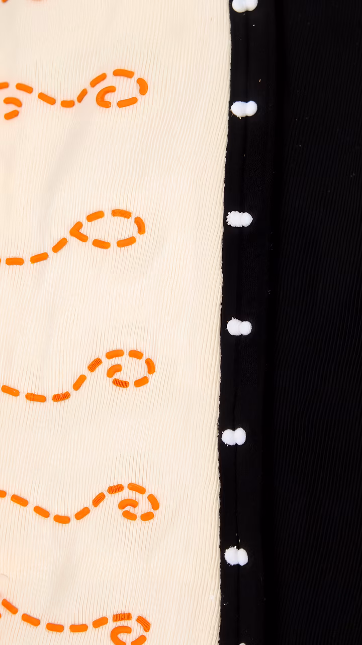 Close-up of embroidered fabric with orange thread patterns on cream background.