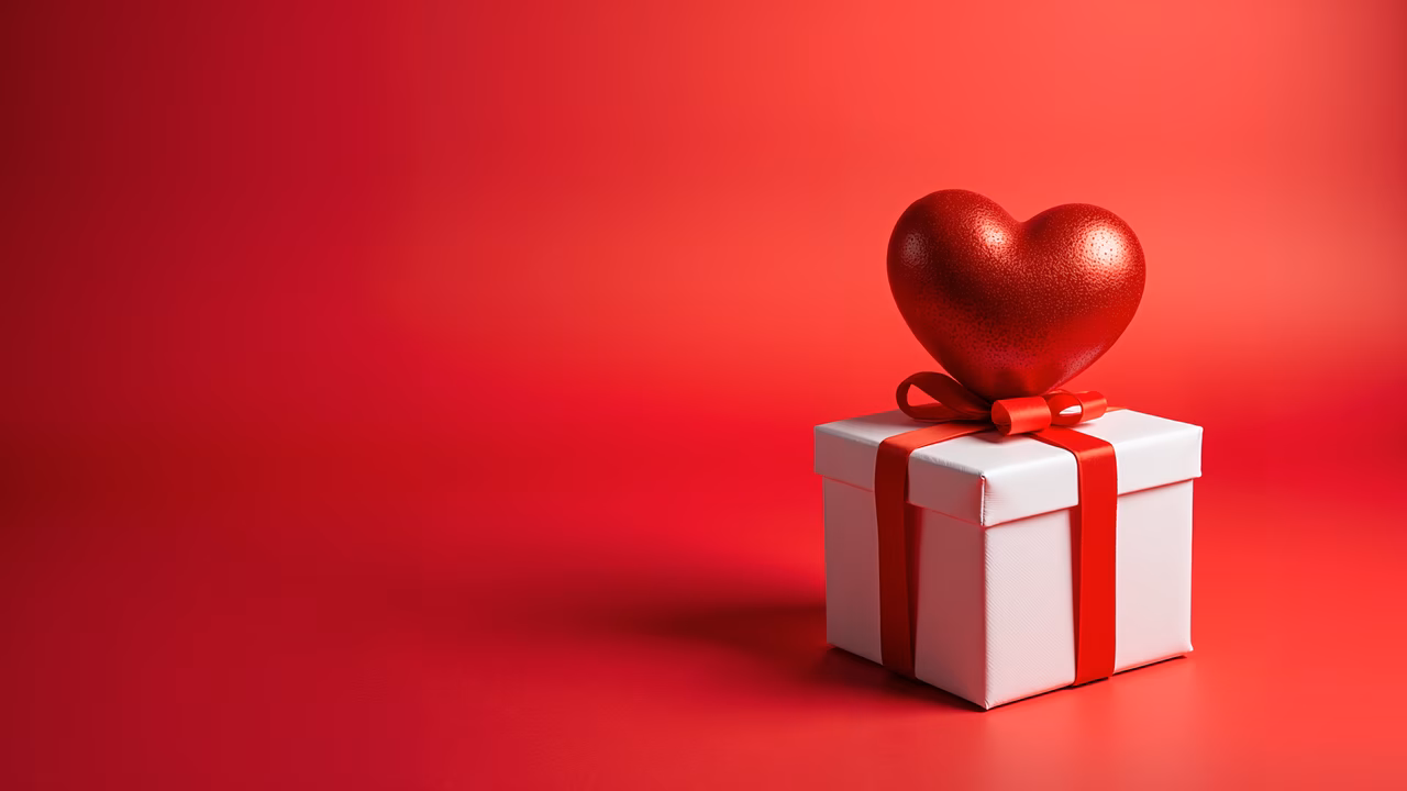 Heart-shaped gift box with red ribbon on a red gradient background, celebrating Valentine's Day.