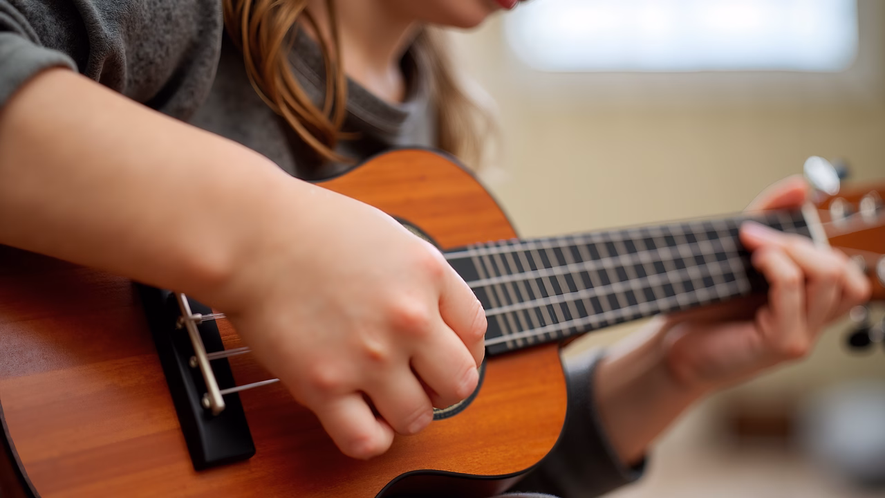 Close-up of hands playing ukulele in a cozy indoor setting.