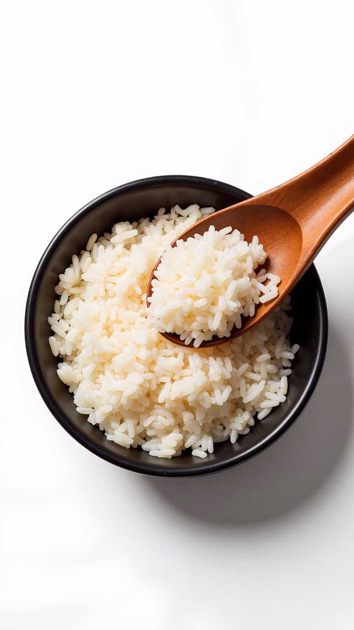 Close-up of freshly cooked white rice in a dark bowl with a wooden spoon.