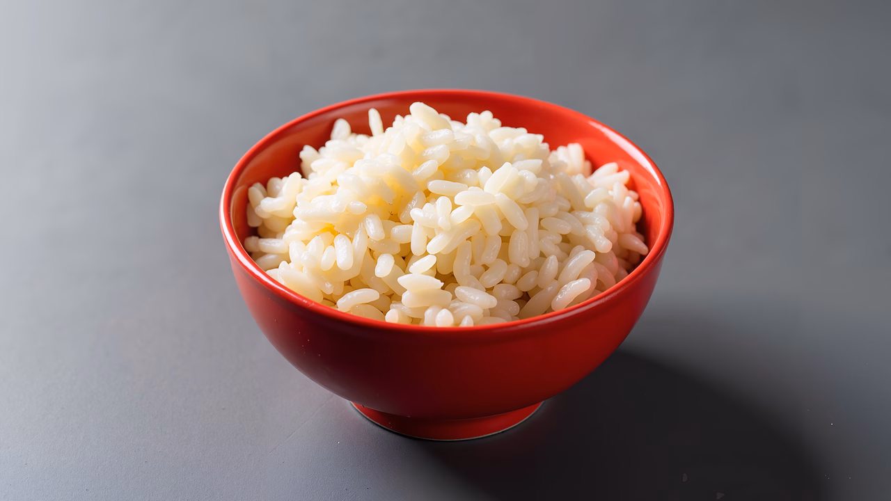 Close-up of fluffy white rice in a red bowl, neutral background.