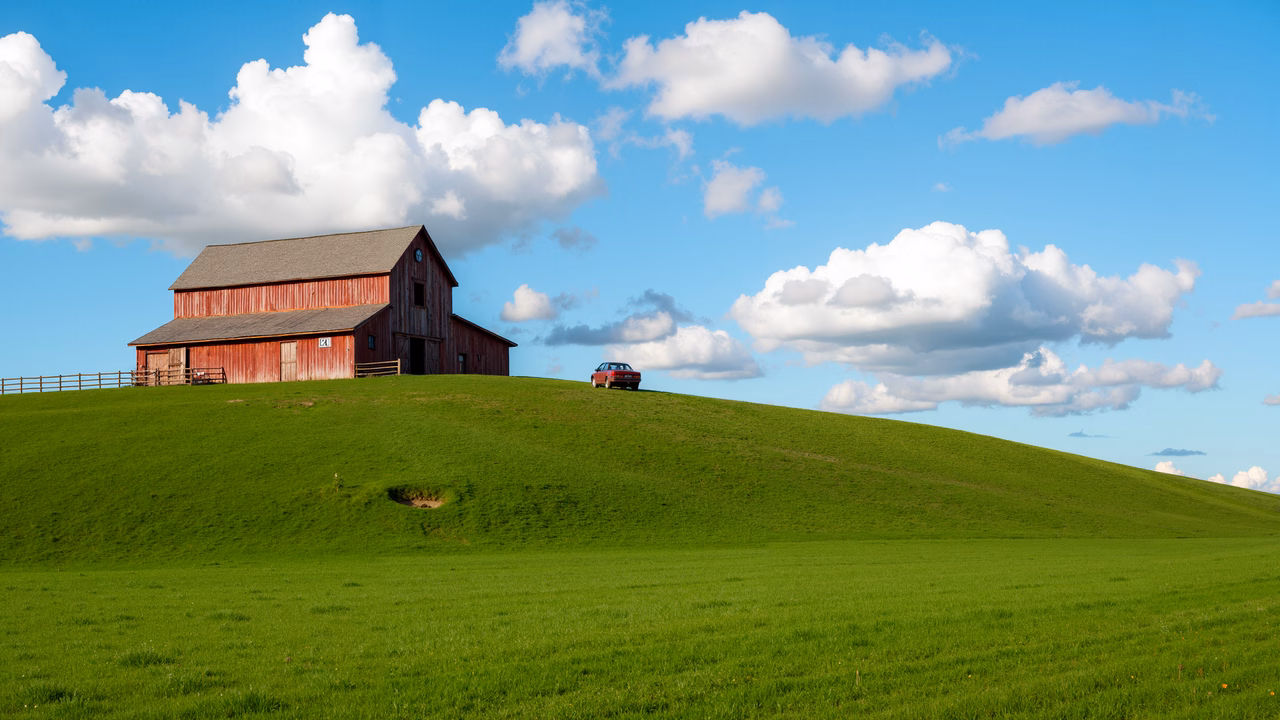 Classic red barn on vibrant green hill under a bright blue sky.