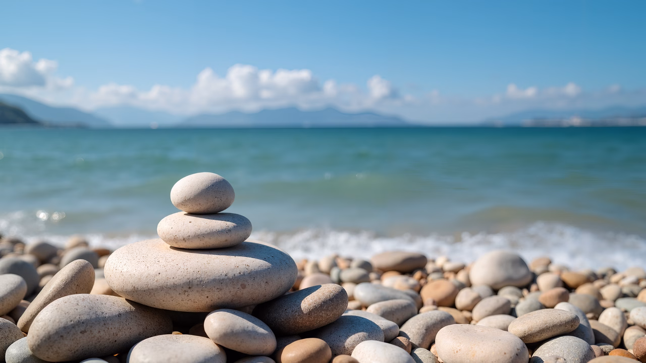 Stacked pebbles on a pebble beach with calm sea and sky.