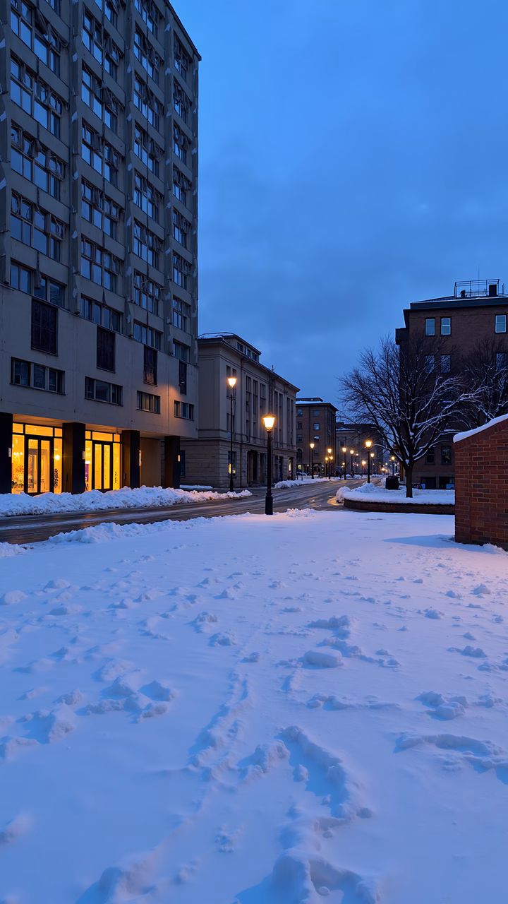 A tranquil winter evening in an urban setting with snow-covered streets and glowing streetlights.