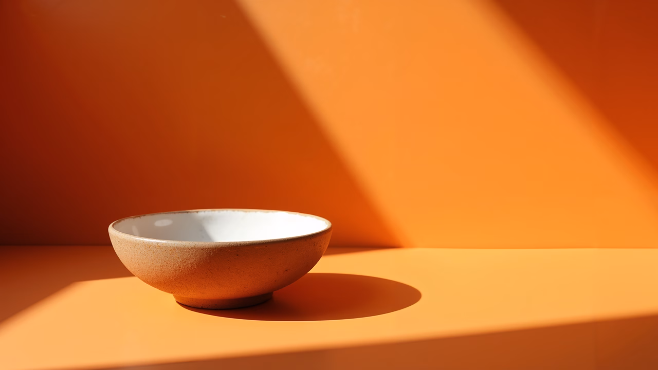 Minimalist bowl on vibrant orange background, serene still life.