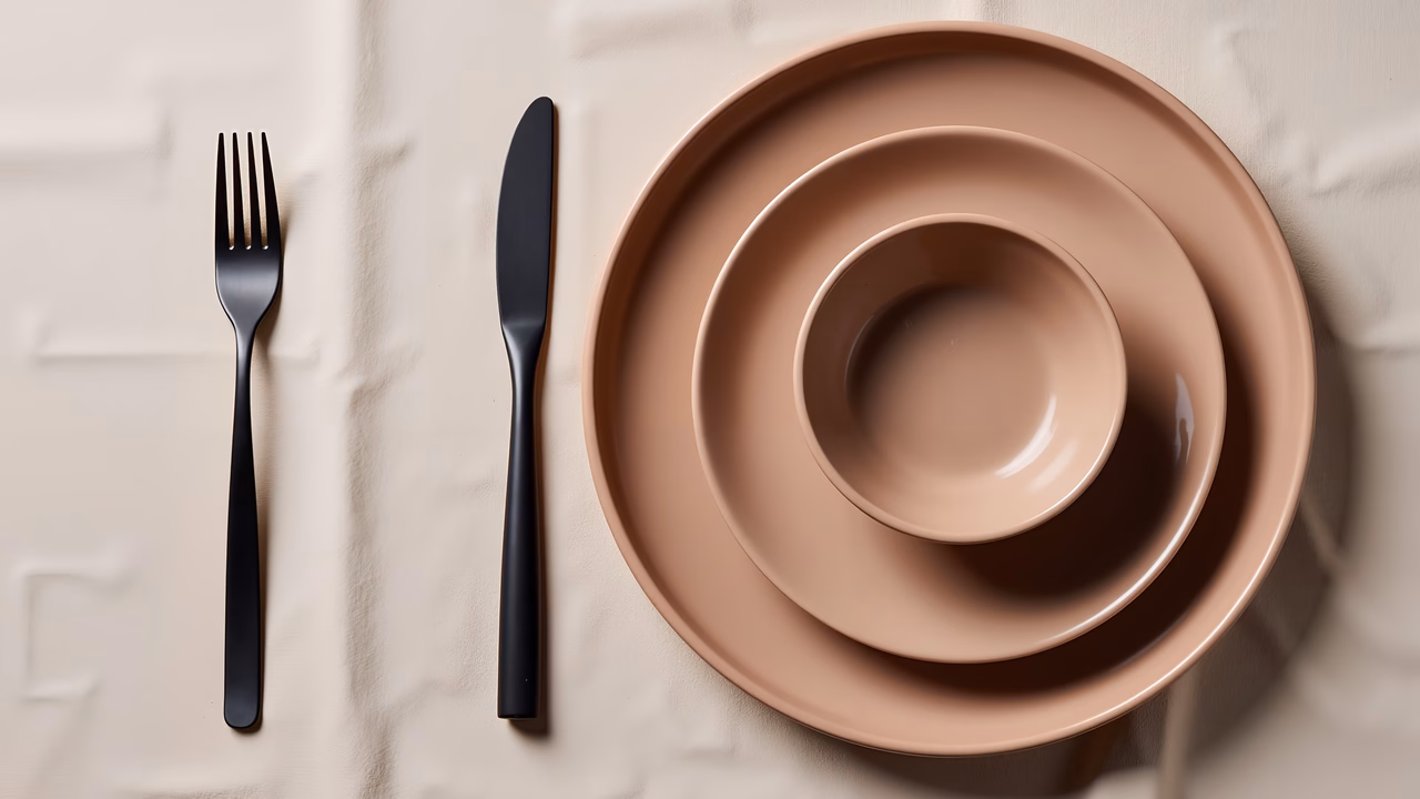 Sleek black cutlery and beige nesting plates on a textured background.
