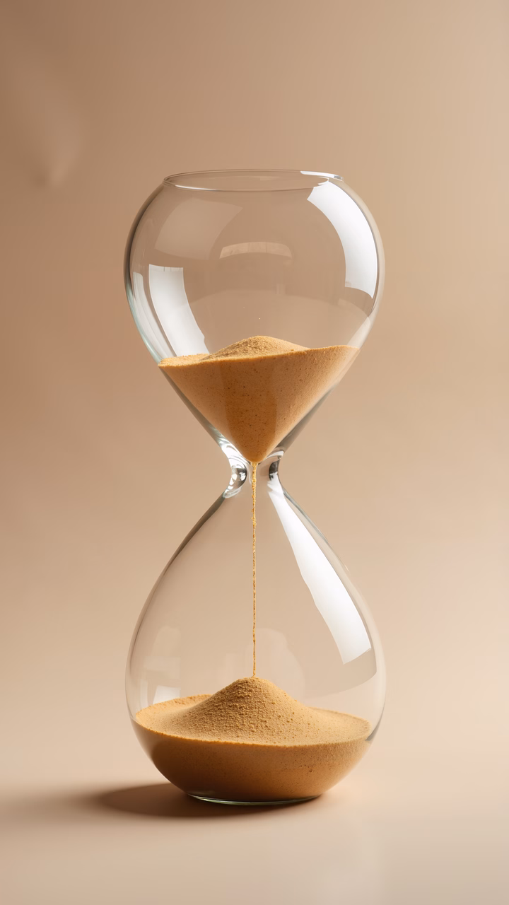 Close-up of a glass hourglass with flowing sand, symbolizing time passing.
