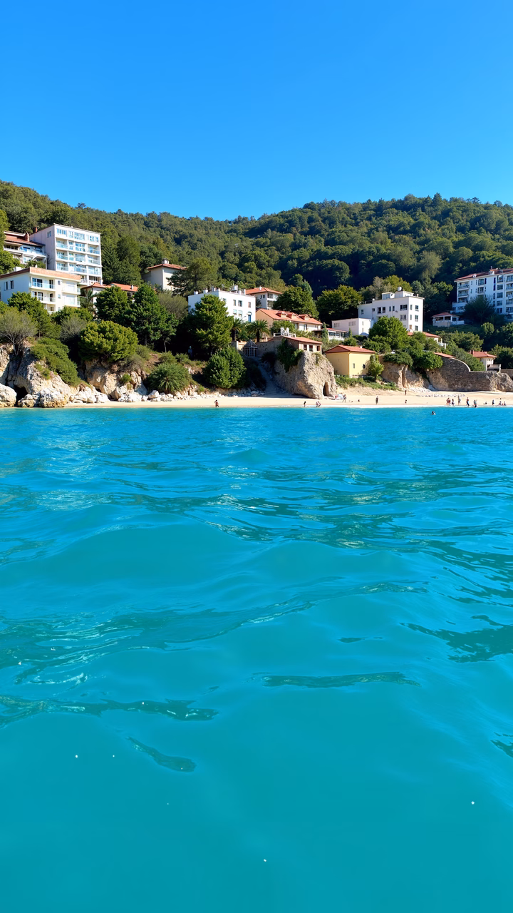Crystal-clear turquoise waters meet a peaceful beach with white buildings and red roofs.