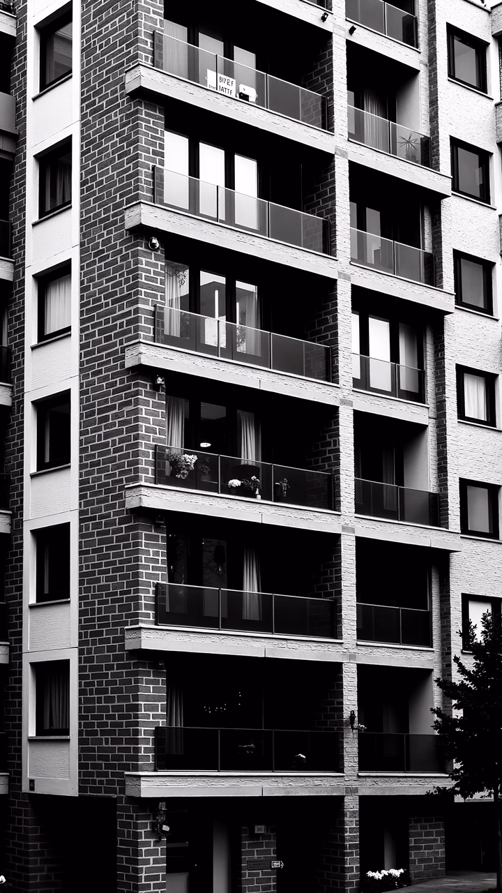 Black-and-white architectural photograph of a brick building with uniform balconies and glass railings.