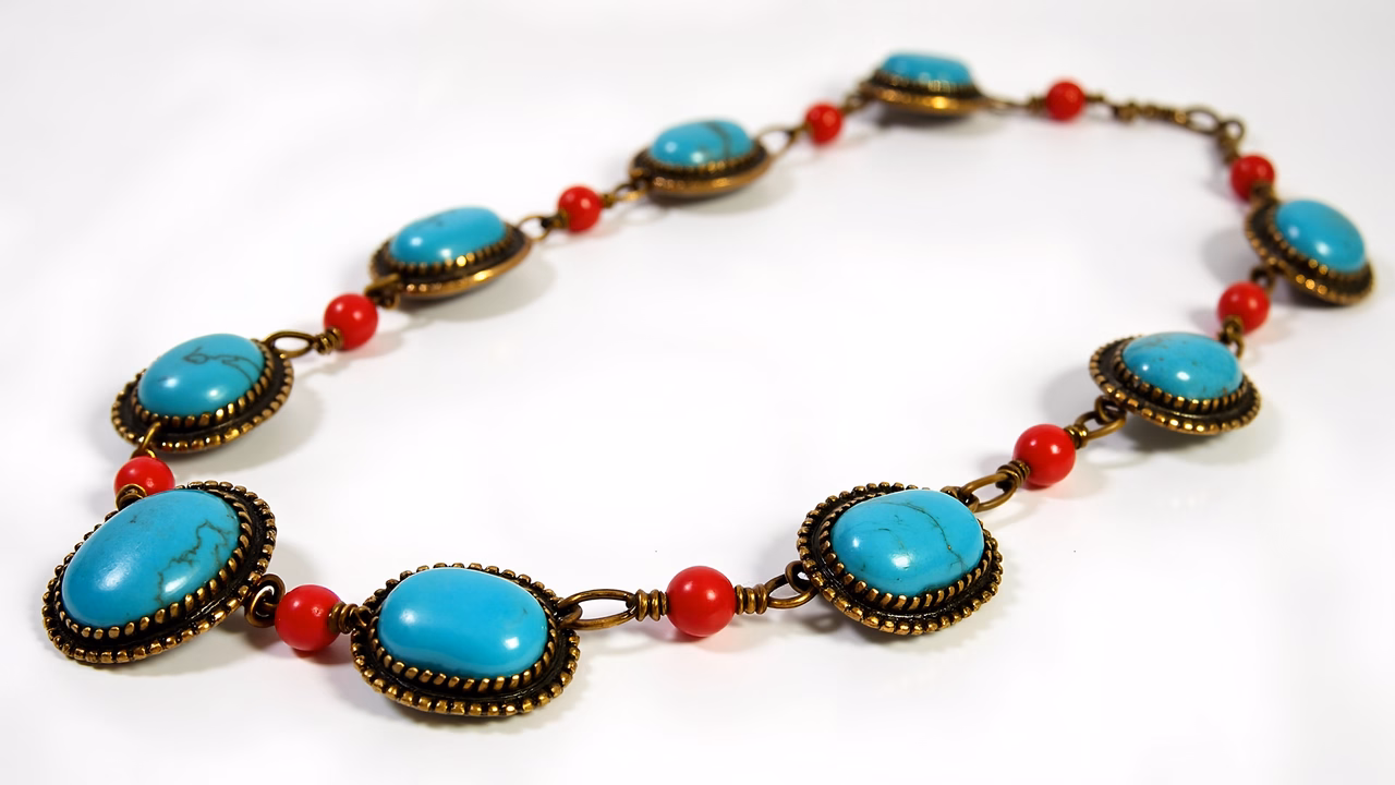Elegant turquoise beaded necklace with gold accents and red beads on a white background.