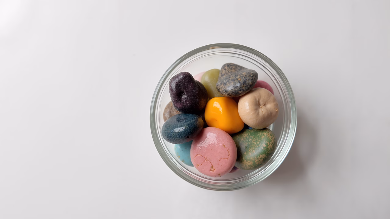 Vibrant rocks in a clear glass bowl on a white background.