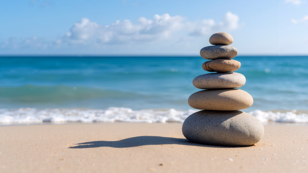 Stacked stones on a peaceful beach with ocean waves and blue sky.