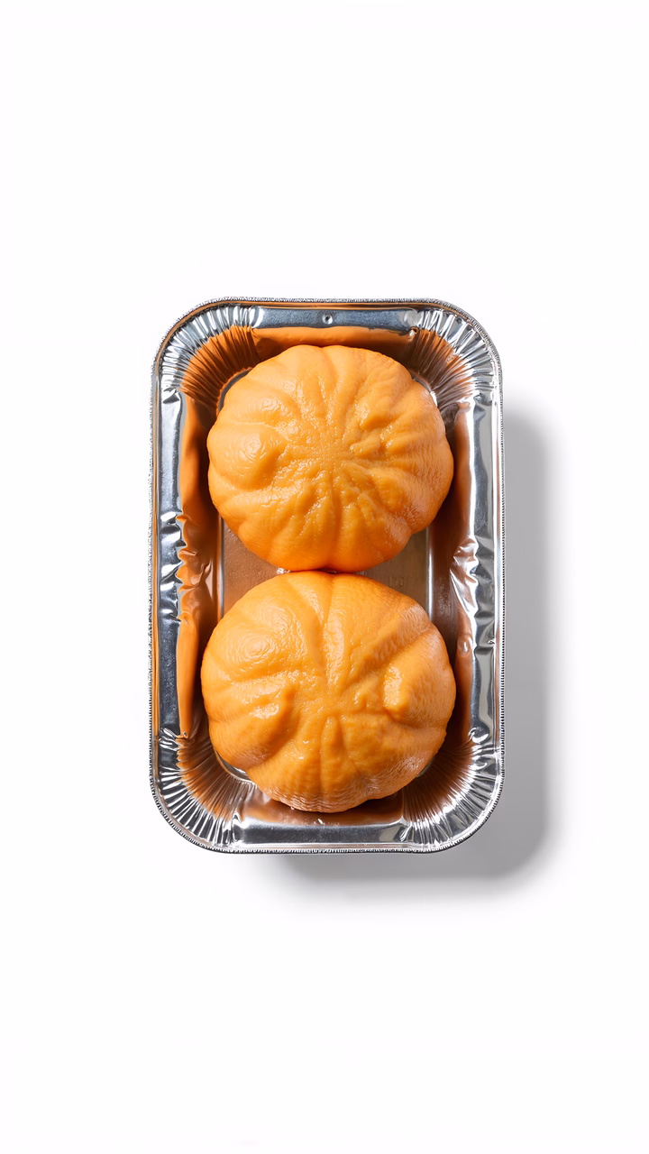 Two pumpkin-shaped pastries in a metallic tray, minimalist food photography.