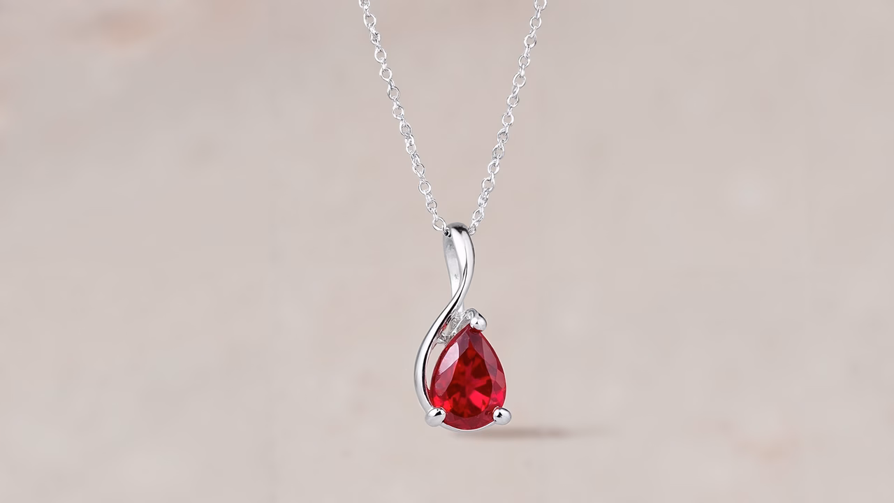 Close-up of a red teardrop pendant with a silver chain, set against a neutral background.