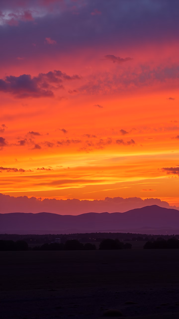 Vibrant sunset over rolling hills, capturing the transition from purple to orange hues.